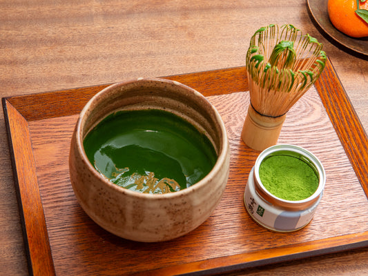 Matcha green tea set on a wooden tray with a bowl, whisk, and container of matcha powder. Koicha