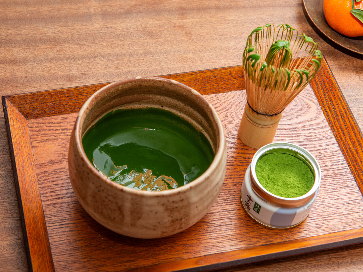 Matcha green tea set on a wooden tray with a bowl, whisk, and container of matcha powder. Koicha
